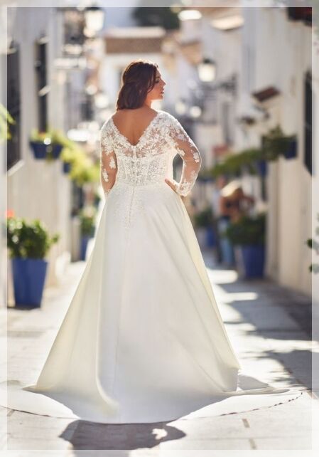 Tres Chic ME26309 - Elegant en vrouwelijk, deze plus-size trouwjurk met een V-stijl voor- en achterkant, ontworpen met fijne kanten applicaties die bij de taille eindigen en de prachtige lange mouwen sieren. De rok is ontworpen met meerdere lagen zacht vloeiende mikado over satijn voor een comfortabel gevoel.